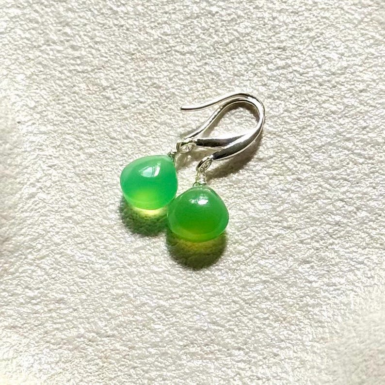 May include: A pair of silver earrings with green gemstone drops. The earrings are teardrop shaped and have a simple design.
