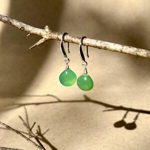 May include: A pair of silver dangle earrings with green gemstone drops. The earrings are hanging from a branch.