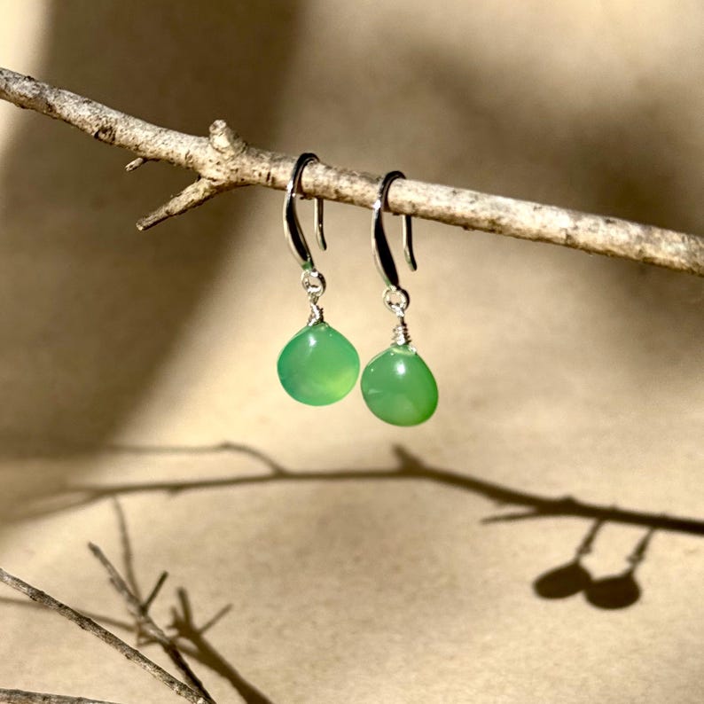 May include: A pair of silver dangle earrings with green gemstone drops. The earrings are hanging from a branch.