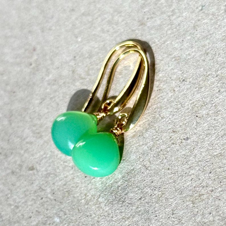 May include: A pair of gold earrings with green gemstone drops. The earrings have a simple, elegant design.