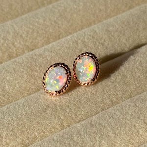 May include: A pair of oval opal stud earrings. The opals have a white base with flashes of orange, yellow, and green. The earrings are set in a rose gold twisted rope design.