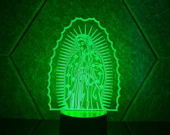 May include: A green LED night light depicting a detailed outline of a religious figure. The figure is surrounded by a radiant halo and stars. The light sits on a black base, reflecting on the surface below. The background is a textured green.