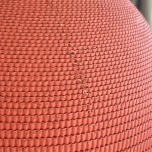 May include: Close-up of a red, textured, rubber ball. The ball has a repeating pattern of small, raised circles.