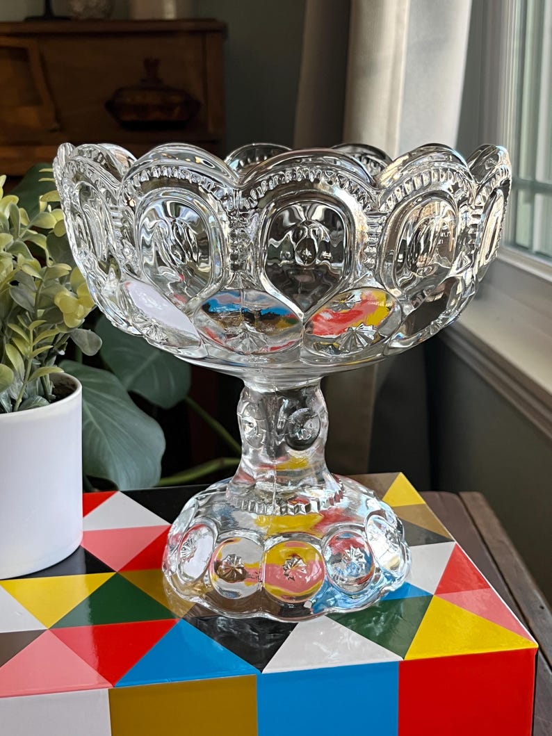 Op de afbeelding: Een glazen kom met een gegolfde rand en een voet. De kom heeft een patroon van kleine cirkels en sterren.
