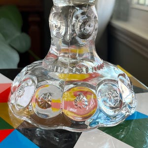 Op de afbeelding: Een glazen voetstuk voor een taart met een gegolfde rand en een voet met een herhalend patroon van cirkels. De voet heeft een getextureerd oppervlak met een subtiele iriserende glans.