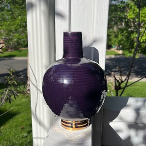 May include: A deep purple ceramic vase with a round body and a gold trim around the base.