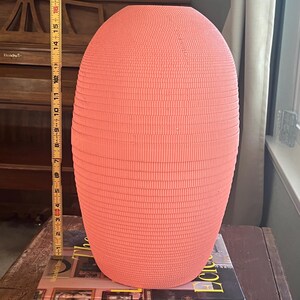 May include: A coral pink ceramic vase with a textured, ribbed surface. The vase is sitting on top of two books, "The Life Eclectic" and "modernstarts".