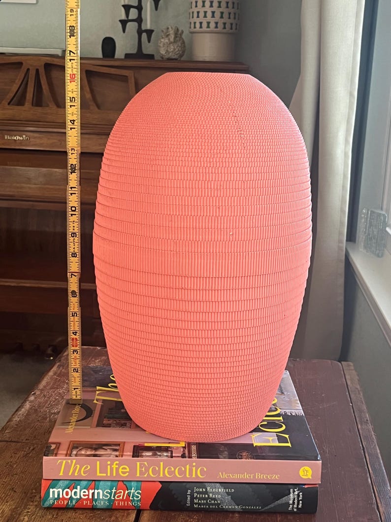 May include: A coral pink ceramic vase with a textured, ribbed surface. The vase is sitting on top of two books, "The Life Eclectic" and "modernstarts".