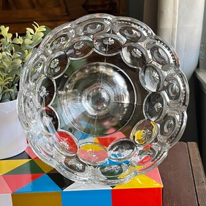 Op de afbeelding: Een glazen kom met een gegolfde rand en een reli&euml;fpatroon van kleine cirkels. De kom is leeg en lijkt vintage te zijn.