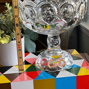 Op de afbeelding: Een glazen snoepschotel met een gegolfde rand en een voet. De schotel heeft een stervormig patroon en is versierd met kleine, verhoogde stippen.