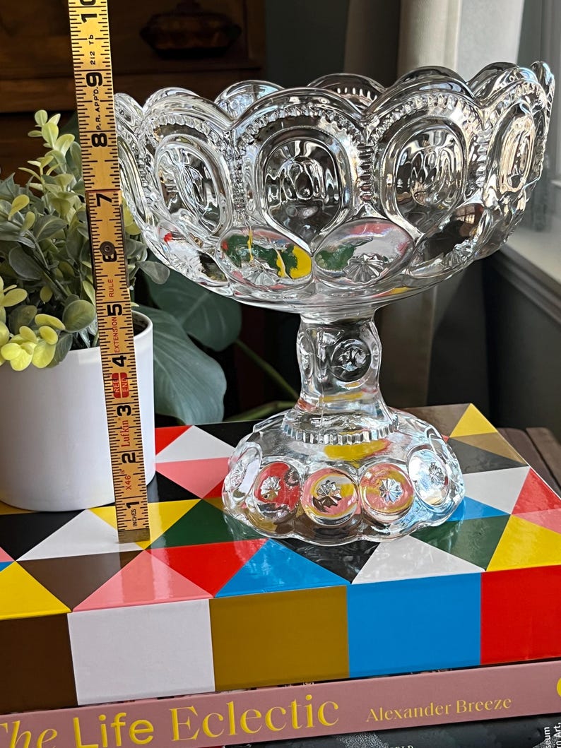 Op de afbeelding: Een glazen snoepschotel met een gegolfde rand en een voet. De schotel heeft een stervormig patroon en is versierd met kleine, verhoogde stippen.
