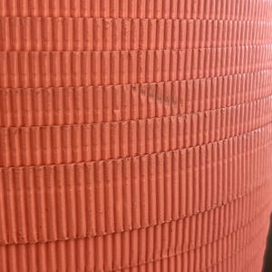 May include: A close-up of a large, orange, cylindrical object with a corrugated surface. The object is made of a textured material and has a smooth, rounded top.