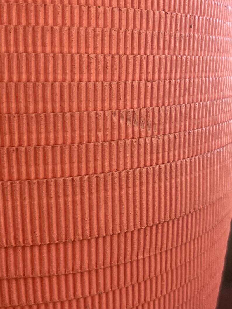 May include: A close-up of a large, orange, cylindrical object with a corrugated surface. The object is made of a textured material and has a smooth, rounded top.