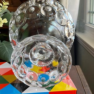 Op de afbeelding: Een glazen snoepschotel met een rond, gewelfd deksel en een gegolfde basis. De schotel is versierd met een patroon van reli&euml;f cirkels.