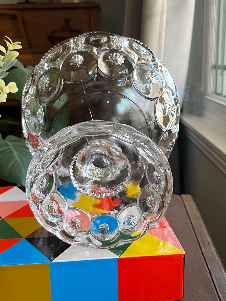 Op de afbeelding: Een glazen snoepschotel met een rond, gewelfd deksel en een gegolfde basis. De schotel is versierd met een patroon van reli&euml;f cirkels.