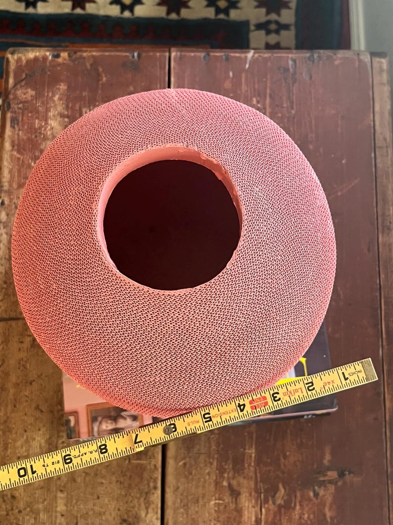 May include: A large, pink, round vase with a textured surface and a wide opening at the top. The vase is approximately 7 inches in diameter.