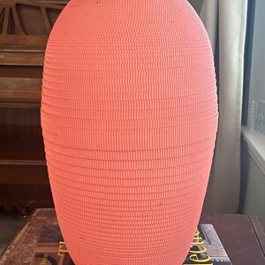 May include: A large, pink, ceramic vase with a textured, ribbed surface. The vase is oval shaped and has a smooth, rounded top.