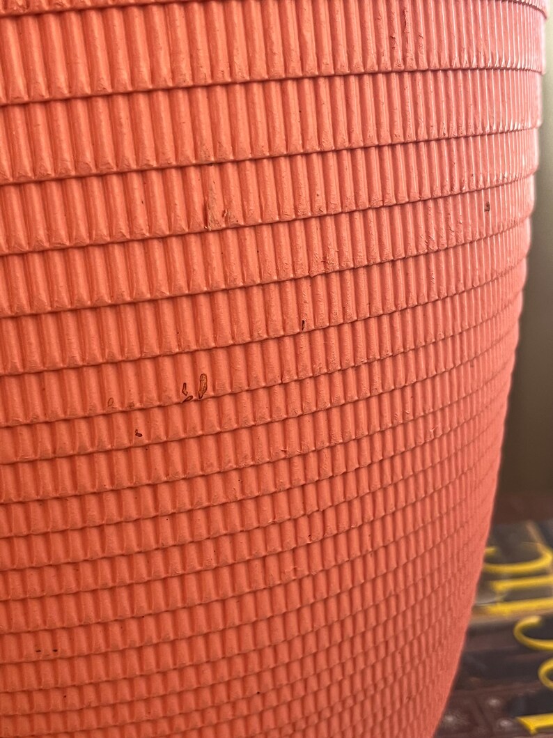May include: Close-up of a bright orange, corrugated cardboard planter. The planter has a rounded shape and a textured surface.