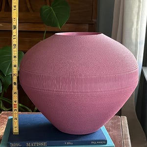 May include: A large, pink ceramic vase with a textured surface. The vase is sitting on top of three books.