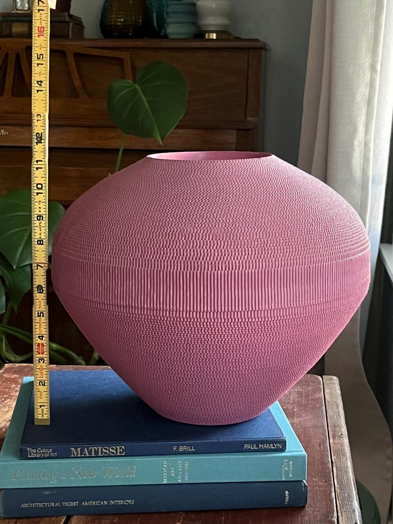May include: A large, pink ceramic vase with a textured surface. The vase is sitting on top of three books.