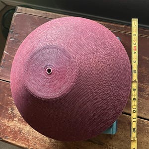 May include: A large, round, burgundy-colored bowl with a textured surface. The bowl is approximately 13 inches in diameter.