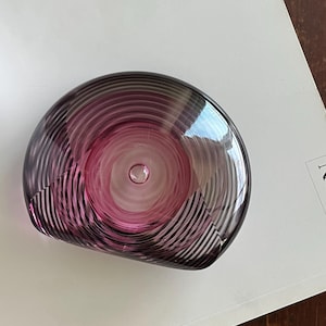 Pode incluir: Uma tigela de vidro rosa com um design de espiral. A tigela é semicircular e tem um acabamento liso e brilhante.