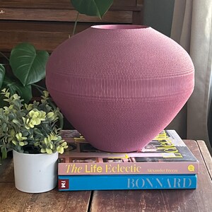 May include: A large, pink, paper mache vase with a textured surface sits on top of two books. The top book is titled "The Life Eclectic" and the bottom book is titled "BONNARD".