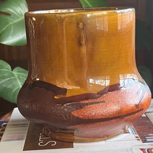 Puede incluir: Un jarrón de cerámica marrón con un esmalte texturizado y craquelado. El jarrón tiene una base ancha y un cuello estrecho, y está decorado con vetas de naranja y marrón.