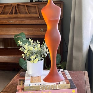 May include: A stack of three books with the title "STYLED" on the top book. The books are on a wooden table with a glass sculpture of a woman in an orange color.
