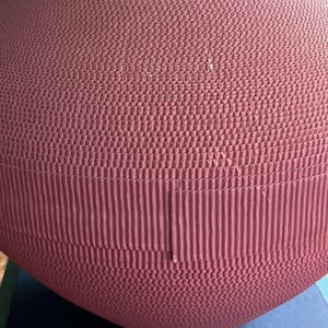May include: A large, round, pink vase made of cardboard. The vase has a textured surface and is made of multiple layers of cardboard.