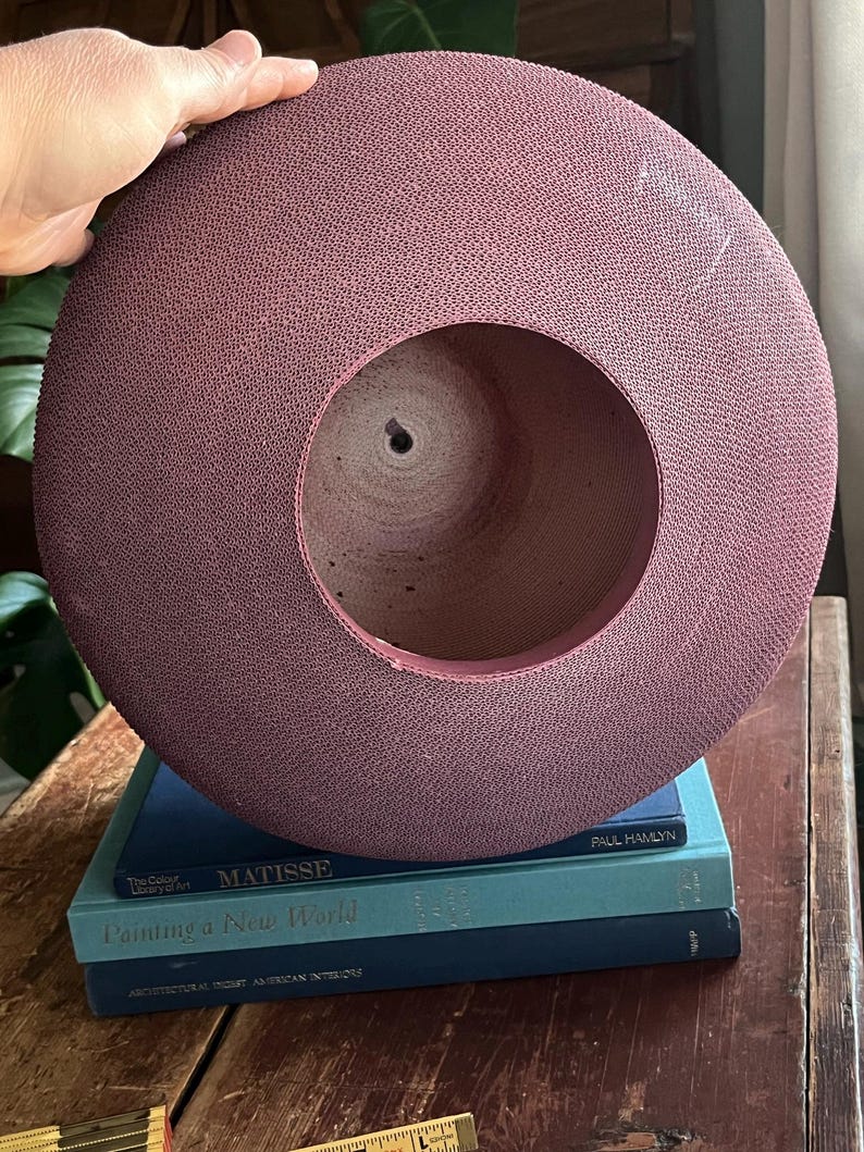 May include: A large, round, purple-colored hat made of woven material. The hat is sitting on top of a stack of three books. The top book has the title "Matisse" and the author "Paul  Hamlvn". The middle book has the title "Painting a New World". The bottom book has the title "Architectural  Art  African  Interiors".