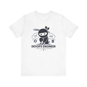 May include: A white short-sleeve t-shirt featuring a dark blue graphic of a crouching ninja. The design includes icons of code brackets, a gear, an infinity symbol, and server racks. Text reads DEVOPS ENGINEER THE CLOUD NINJA with a small star.