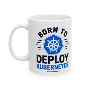 May include: A white ceramic mug featuring a blue and black graphic design. The text reads BORN TO DEPLOY KUBERNETES, centered around a blue hexagon containing a white ship's wheel icon. The design includes horizontal lines on both sides.
