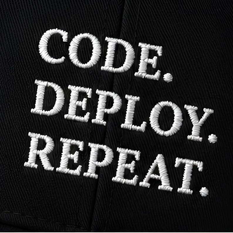 May include: A black fabric surface featuring white embroidered text arranged in three horizontal lines. The text reads "CODE." on the first line, "DEPLOY." on the second line, and "REPEAT." on the third line, all in a bold, sans-serif font.