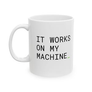 以下が含まれることがあります： 黒い文字で「IT WORKS ON MY MACHINE」と書かれ、最後に小さな緑色のアンダースコアが付いた白いセラミック製のマグカップ。マグカップは標準的な円筒形で、左側に湾曲したハンドルがあり、無地の白い背景の前に配置されています。