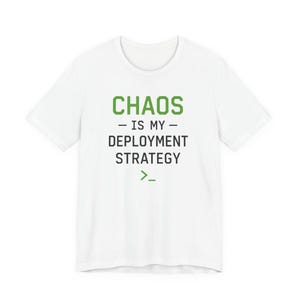 Puede incluir: Una camiseta blanca de manga corta con el texto en verde y negro "CHAOS - IS MY - DEPLOYMENT STRATEGY" seguido de un símbolo de línea de comandos verde ">_" centrado en el pecho. La camiseta tiene cuello redondo y un corte estándar.