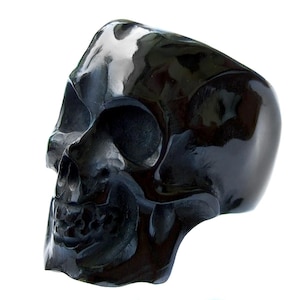 May include: A black skull ring made of polished obsidian. The ring is detailed with a realistic skull design, including eye sockets, a nose, and a mouth.