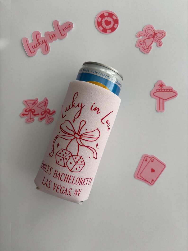 Pode incluir: Um refrigerador de latas branco com fundo rosa e texto vermelho que diz "Lucky in Love" com um la&ccedil;o e dados. O texto abaixo diz "Emily's Bachelorette Las Vegas, NV".