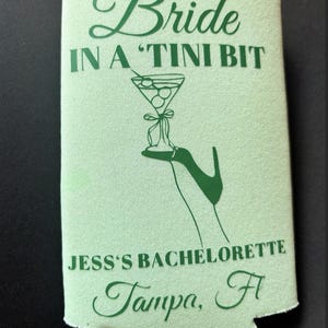 May include: Green and white can cooler with the text "Bride in a 'Tini Bit" and a martini glass with olives. The text "Jess's Bachelorette Tampa, Fl" is also printed on the cooler.