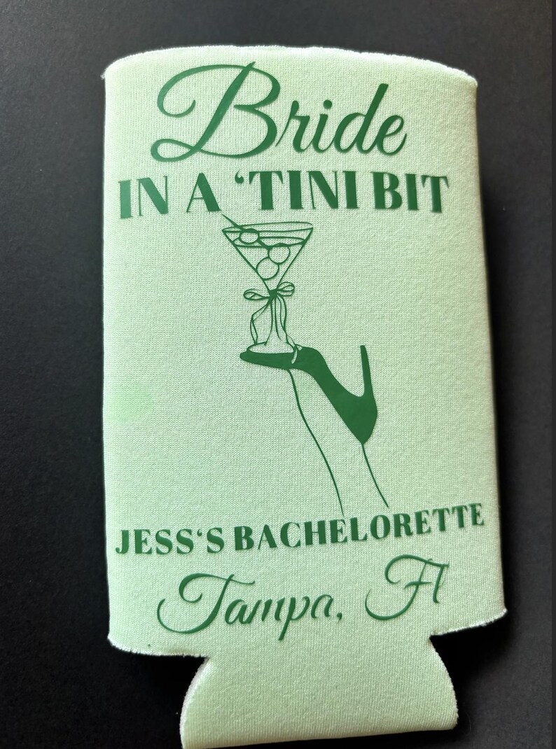 May include: Green and white can cooler with the text "Bride in a 'Tini Bit" and a martini glass with olives. The text "Jess's Bachelorette Tampa, Fl" is also printed on the cooler.