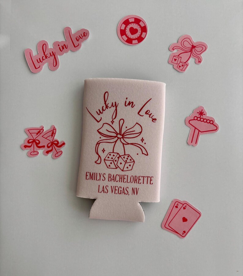 Pode incluir: Frigor&iacute;fico de latas rosa e vermelho com o texto "Lucky in Love" e "Emily's Bachelorette Las Vegas, NV". O refrigerador tem um la&ccedil;o rosa com dados pendurados. H&aacute; v&aacute;rios adesivos rosa e vermelhos ao redor do refrigerador, incluindo um cora&ccedil;&atilde;o, dados, uma ta&ccedil;a de martini, uma ficha de cassino e uma placa de cassino.