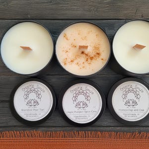 May include: Four black candle jars with lids, each with a different scent. The scents are Brandied Pear Tart, Maple Pumpkin Spice Cake, Honeycrisp and Oak. Each jar has a wooden wick and is handmade in Wisconsin.