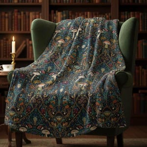 May include: A dark teal throw blanket featuring a repeating pattern of mushrooms and foliage. The blanket is draped over a green armchair. The room has a bookshelf in the background.