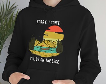 Puede incluir: Sudadera con capucha negra con un gráfico blanco de una escena de lago con puesta de sol y el texto "Lo siento, no puedo. Estaré en el lago."