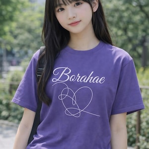 May include: A purple t-shirt with the word "Borahae" in cursive and a white heart design. The shirt is made of a soft material and is suitable for casual wear. The model is wearing a backpack.