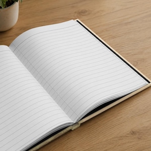 May include: An open notebook with white pages featuring black horizontal lines. The notebook has a light-colored cover and is positioned at an angle, revealing the interior paper layout with clear, evenly spaced ruled lines for writing.