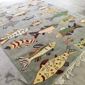 May include: A rectangular rug with a pale grey backdrop, patterned with colourful fish. The fish designs vary in size and colour, including yellow, green, blue, and brown. The rug has a fringed edge, and is suitable for a living room.