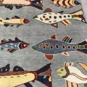 May include: A light blue rug with a repeating pattern of colourful fish. The fish designs feature various colours, including yellow, brown, blue, and green, creating a vibrant and playful aesthetic. The rug is likely made of woven material.