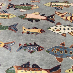 May include: A light blue rug featuring a repeating pattern of colourful fish. The fish vary in size and design, with shades of green, yellow, brown, and blue. The rug's background is a solid, muted blue.