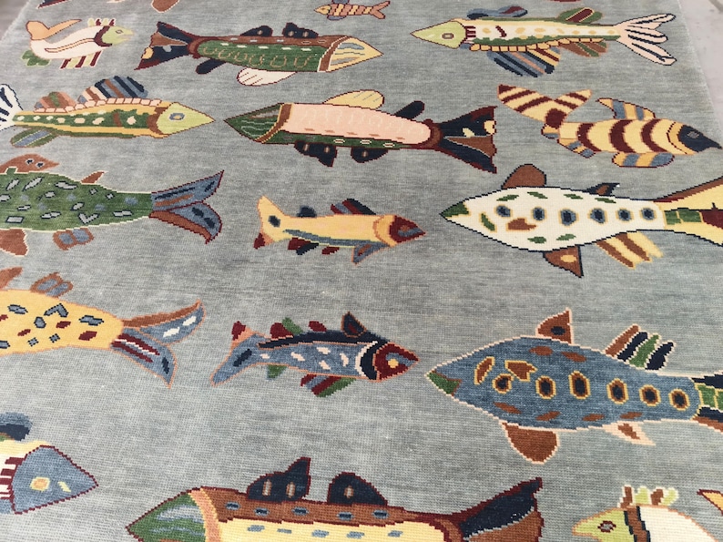 May include: A light blue rug featuring a repeating pattern of colourful fish. The fish vary in size and design, with shades of green, yellow, brown, and blue. The rug's background is a solid, muted blue.